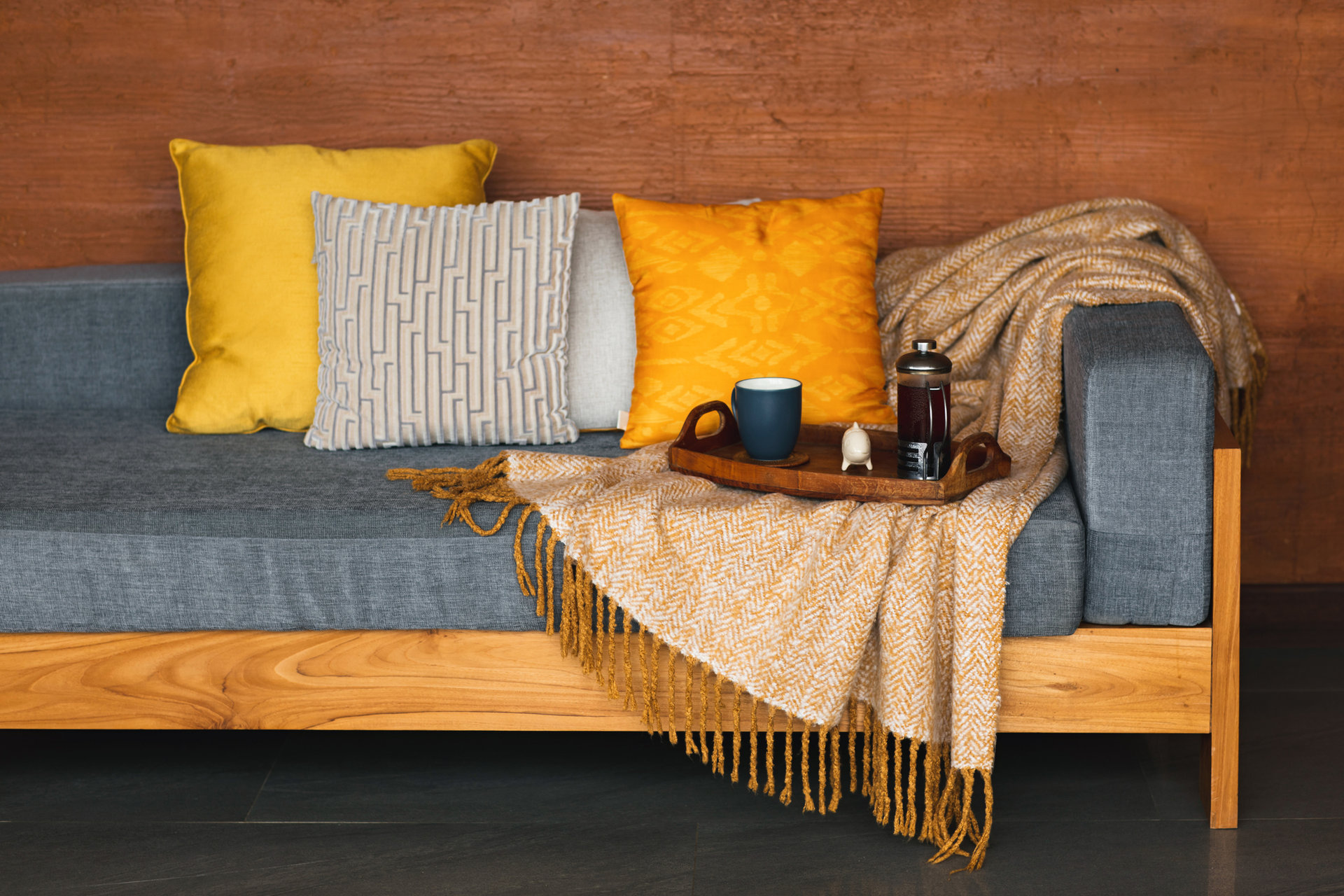 Serving tray with tea on gray sofa with yellow and orange pillows and wool blanket. Warm and cozy weekend at home. Modern and fresh living space. Top view.